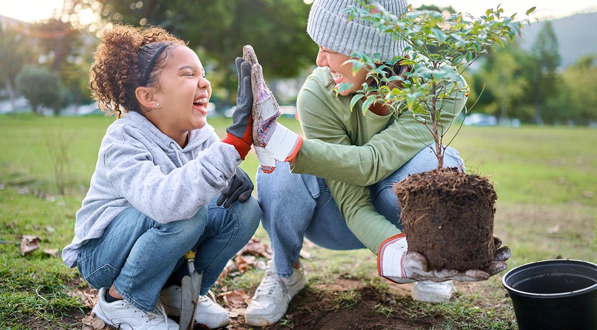 A young girl and woman high five while planting a tree