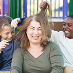 A woman laughs while children play with her hair.