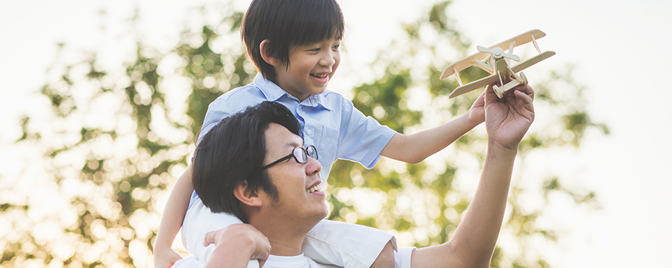 A father and his young son play with a toy airplane together.