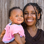 A mother holds her infant child while smiling.