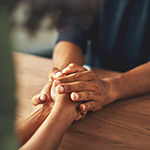 Consoling hands reach across a table to hold another person's hands.