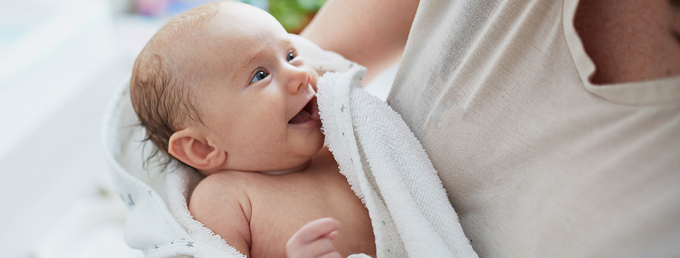 A smiling infant looks up at the woman holding them.