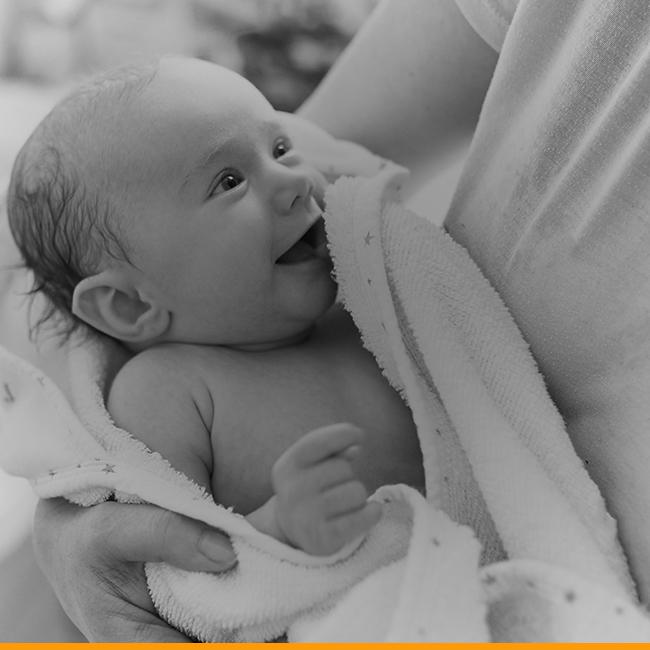 A smiling infant looks up at the person holding them.