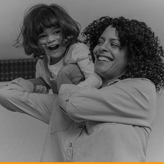 A mother playfully lifts her small daughter up onto her shoulder.